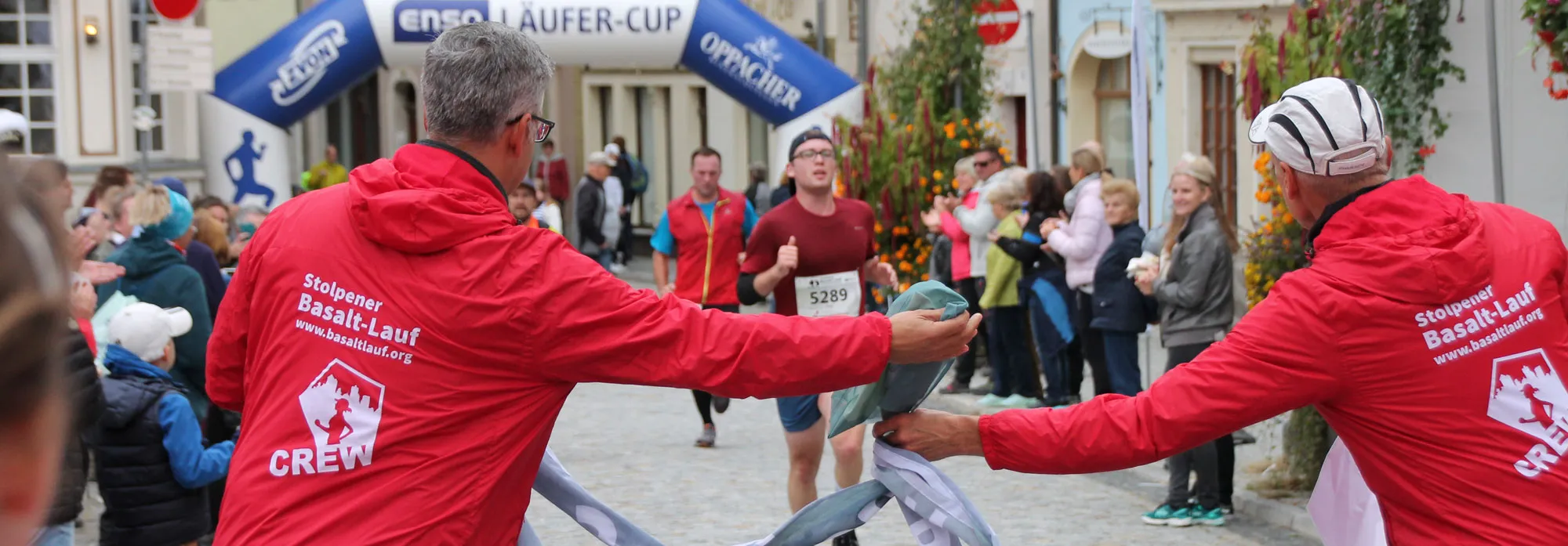 Helfer in roten Crew-Jacken empfangen Läuferinnen und Läufer im Ziel