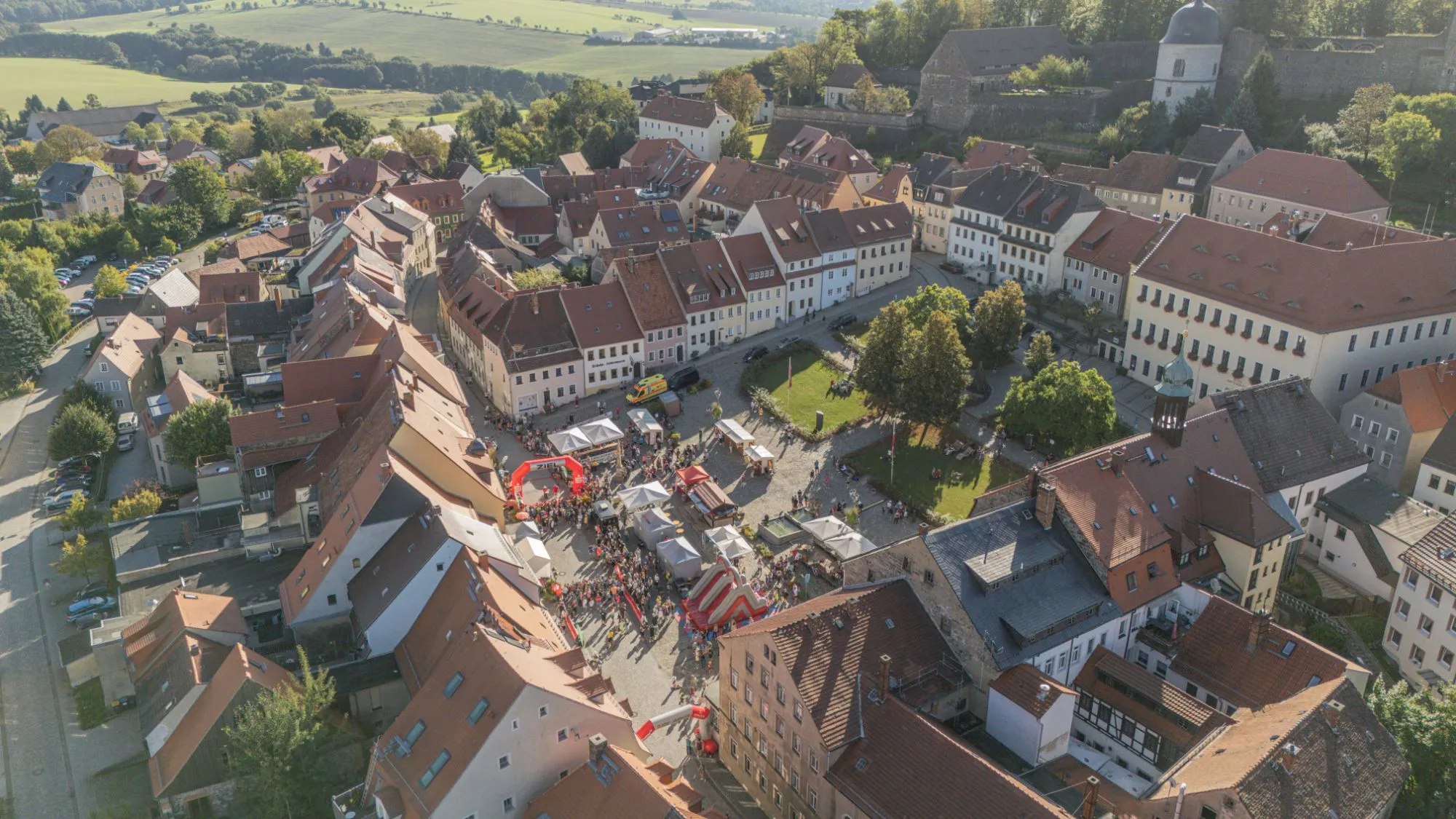 Luftbild vom Stolpener Marktplatz am Lauftag mit Zielbogen, Zelten, Kletterberg und Zuschauern, dahinter die Burg